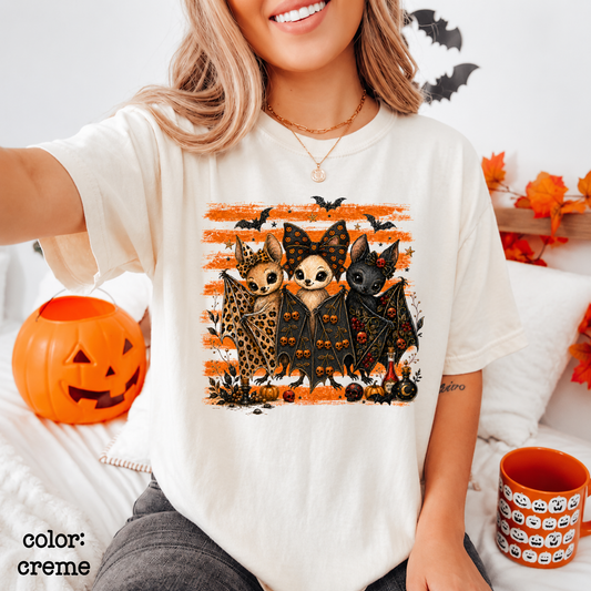 Person wearing a white t-shirt with a Halloween-themed design of cats in costumes, sitting on a couch with pumpkins and a mug.