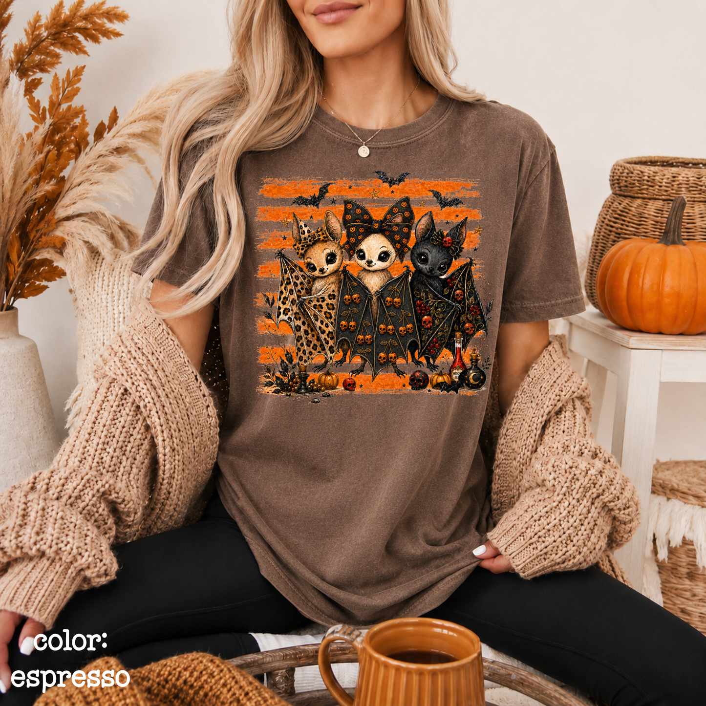Person wearing a brown t-shirt with a cat-themed design, sitting in a cozy room with pumpkins and autumn decorations.