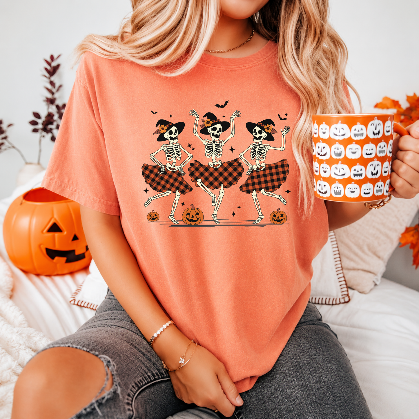 Person wearing a Halloween-themed t-shirt with skeletons and plaid skirts, holding a pumpkin-patterned mug.