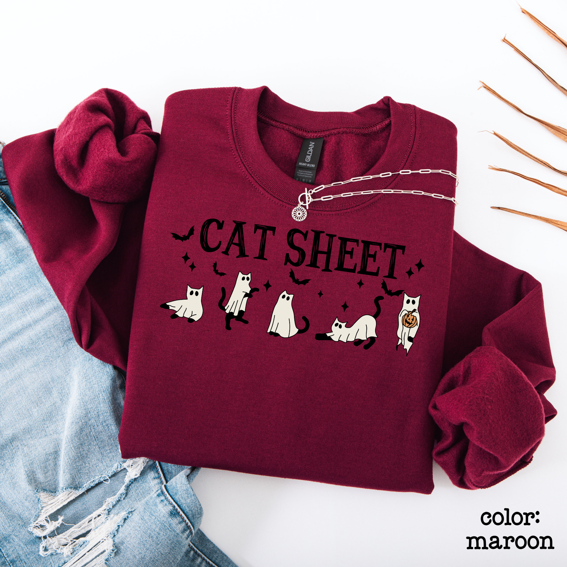 Minimalist style presentation of a Halloween graphic sweater with the bold text "CAT SHEET" surrounded by whimsical ghost and cat elements.