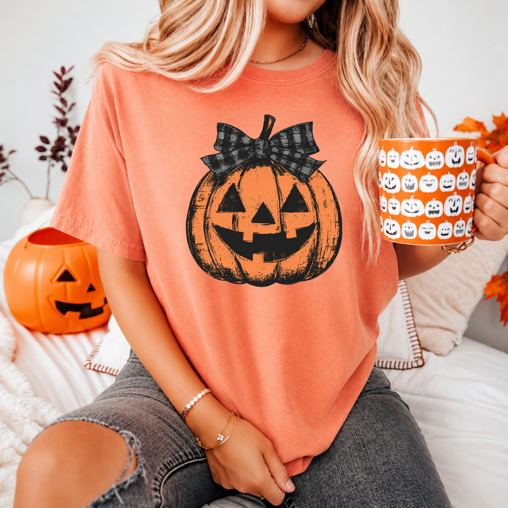 Person wearing a Halloween-themed t-shirt with a pumpkin design, holding a mug with pumpkins, sitting on a couch.
