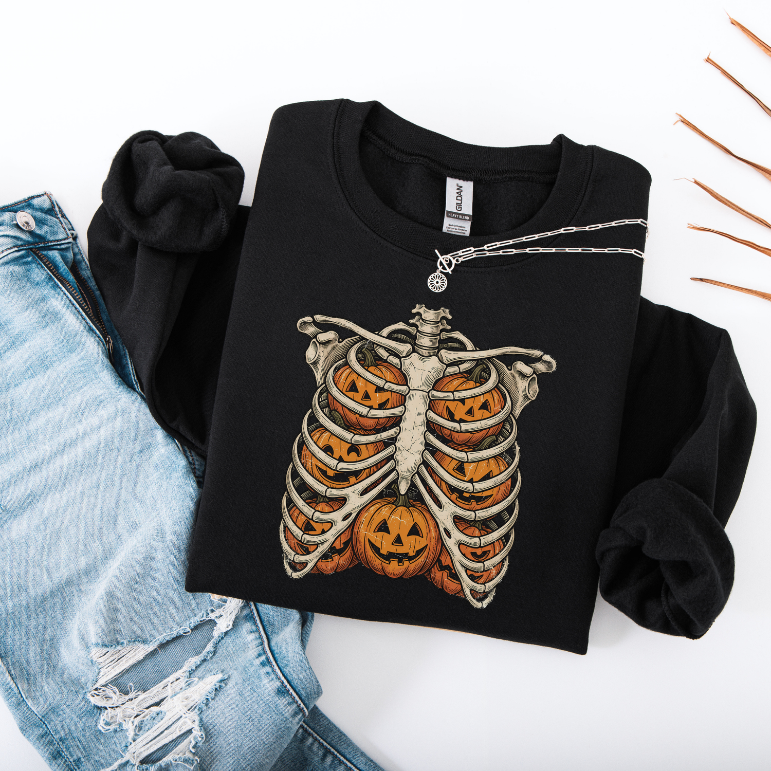 Flat lay of a sand-colored graphic sweatshirt showcasing a black printed skeleton ribcage with an orange jack-o'-lantern glowing inside the center.