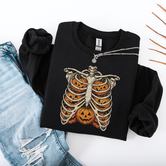 Flat lay of a sand-colored graphic sweatshirt showcasing a black printed skeleton ribcage with an orange jack-o'-lantern glowing inside the center.