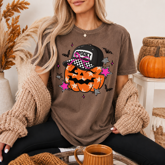 Woman wearing a brown t-shirt with a Halloween-themed design, sitting in a cozy room with pumpkins and autumn decorations.