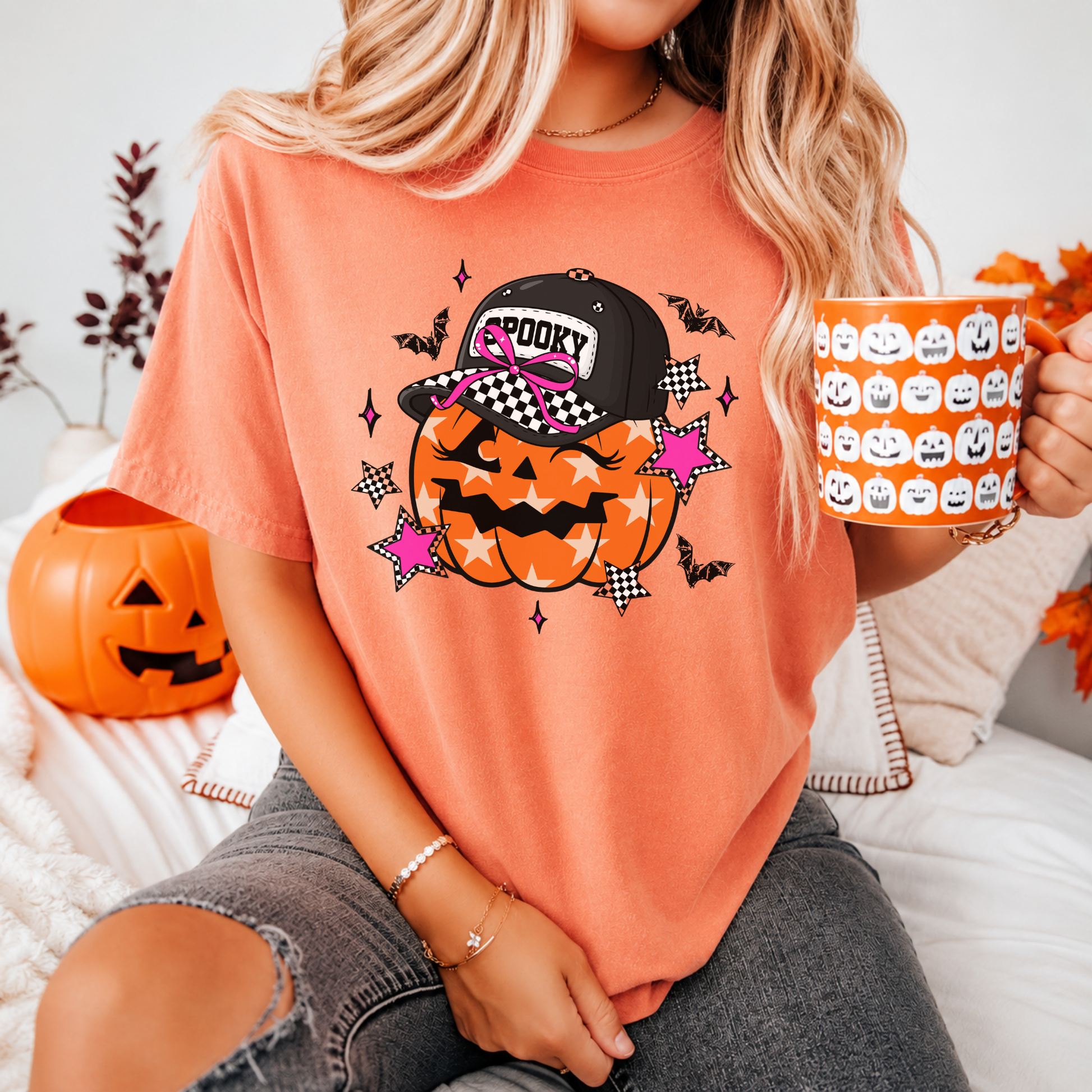 Person wearing a Halloween-themed t-shirt with a pumpkin and cap design, holding a mug with pumpkins, sitting on a couch.