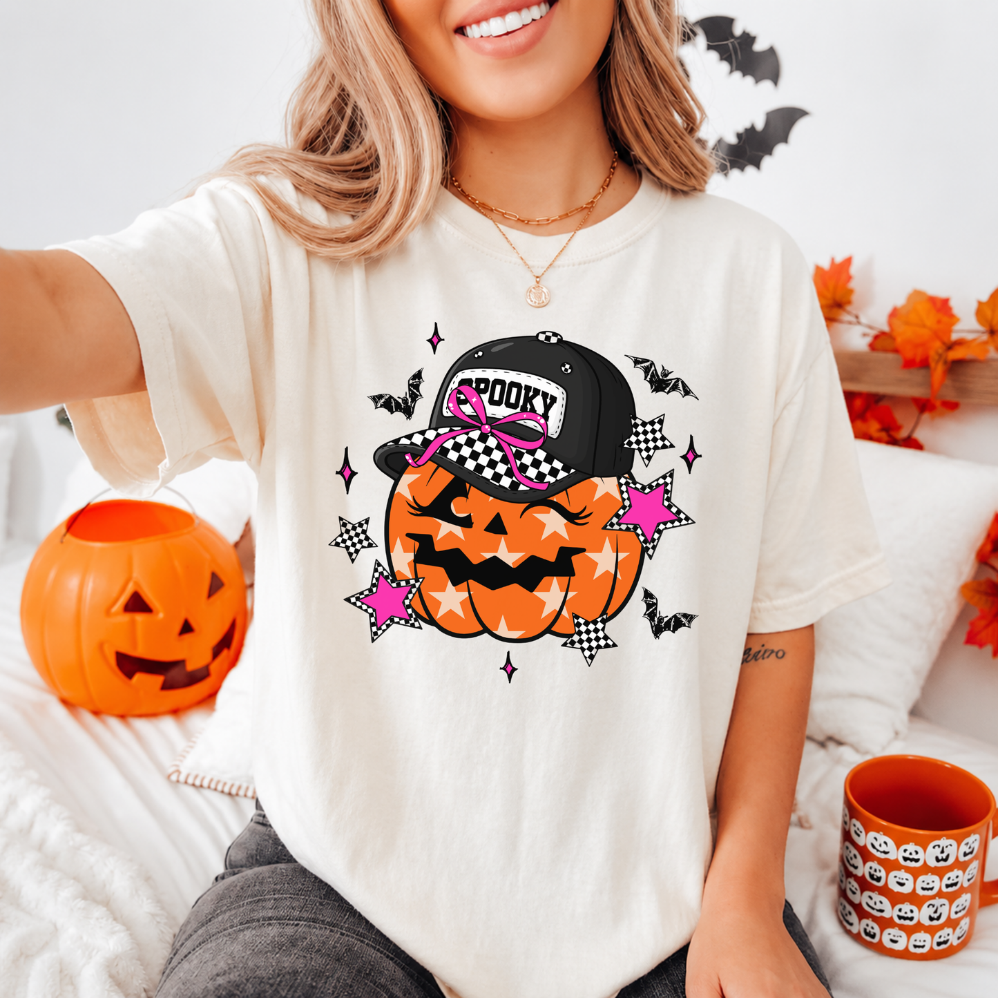 Person wearing a Halloween-themed t-shirt with a pumpkin and witch hat design, surrounded by Halloween decor.